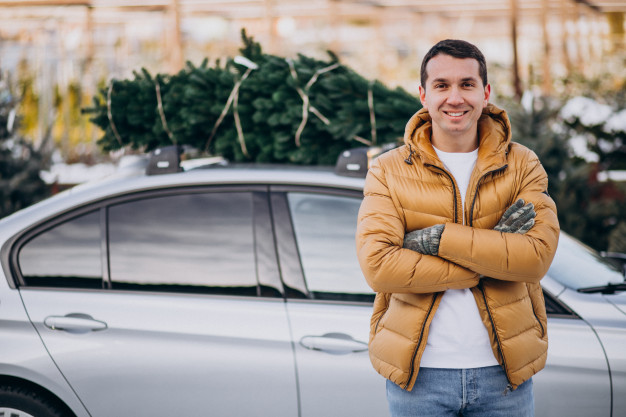 hombre-joven-que-entrega-arbol-navidad-coche_1303-19511