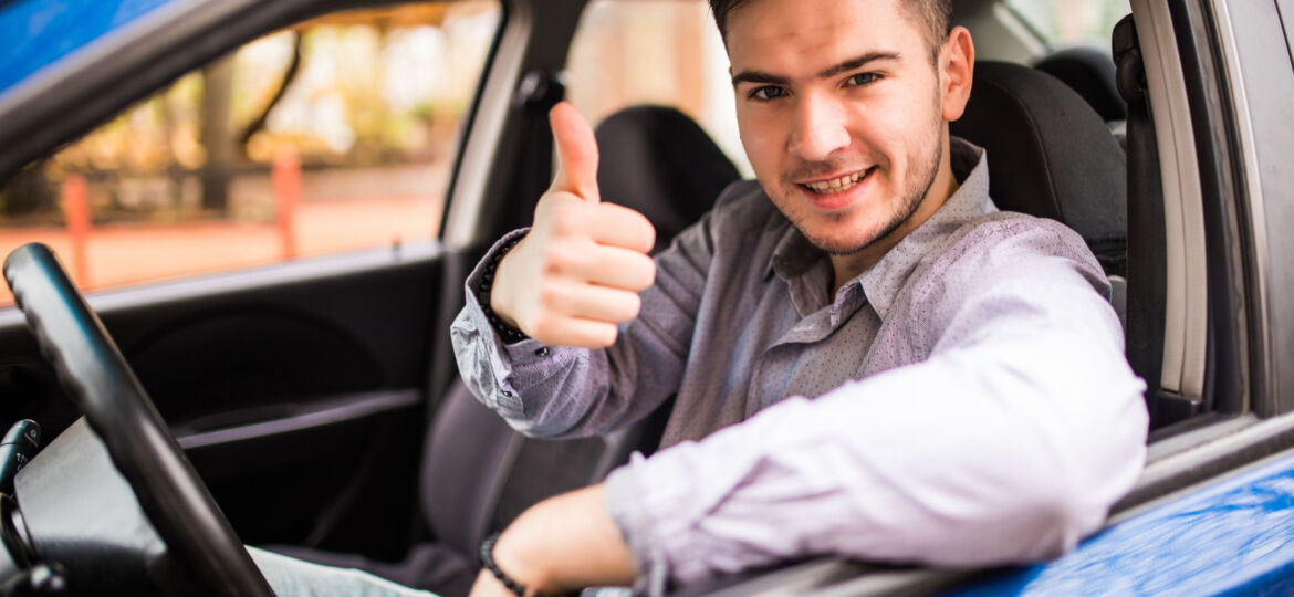 Happy smiling man sitting inside car showing thumbs up. Handsome