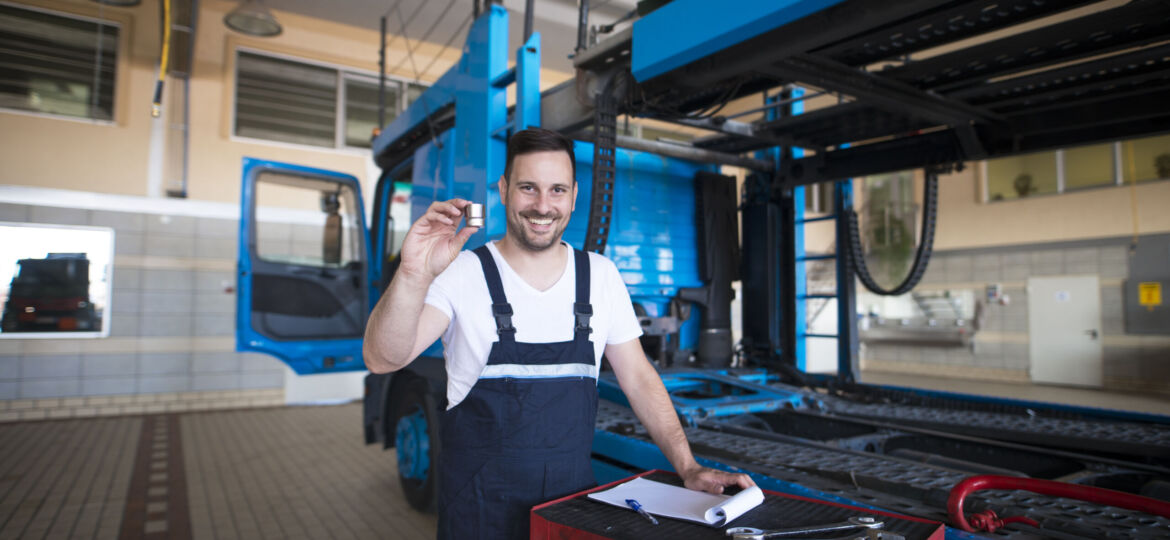 Experienced middle aged truck mechanics holding parts and tools in repair shop by the truck.